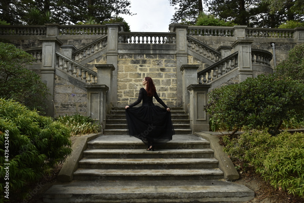 portrait of pretty female model with red hair wearing glamorous gothic black lace ballgown. Posing in a fairytale castle location with staircases portrait of pretty female model with red hair wearing glamorous gothic black lace ballgown. Posing in a fairytale castle location with staircases