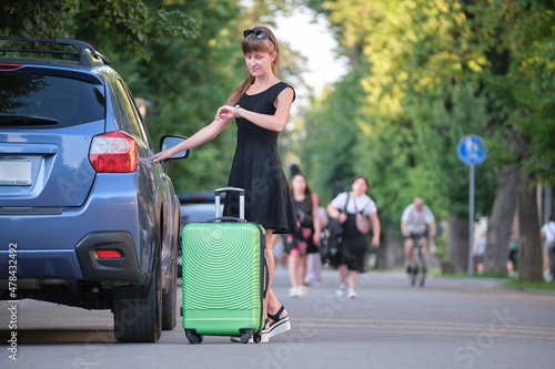 Young woman driver taking out suitcase bag out of her car. Travelling and vacations concept