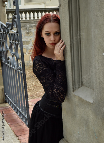  portrait of pretty  female model with red hair wearing glamorous gothic black lace ballgown.  Posing in a fairytale castle location with staircases 