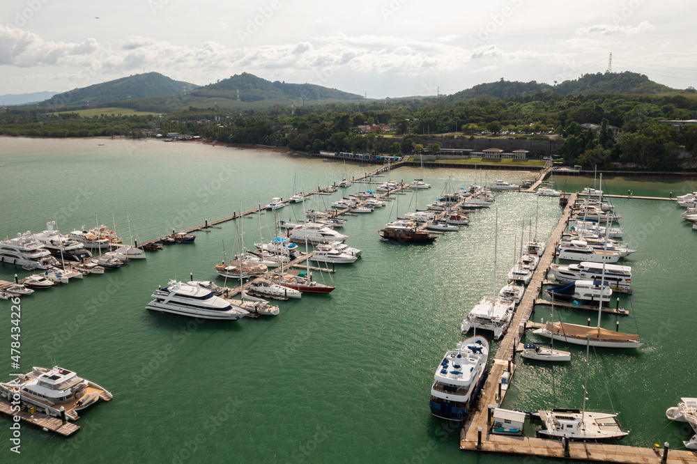 Aerial view of sail boats in marina port in harbor, ocean or bay with blue turquoise seawater in urban city or town, Phuket in travel trip and transportation concept. Top view.