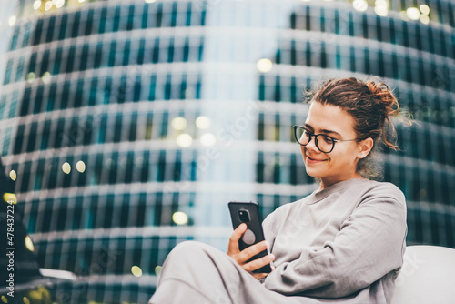 Young woman in glasses looks into smartphone sitting at the stairs. photo