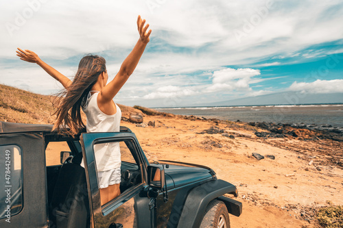 Foto Car road trip travel fun happy woman tourist with open arms at ocean view from sports utility car driving on beach