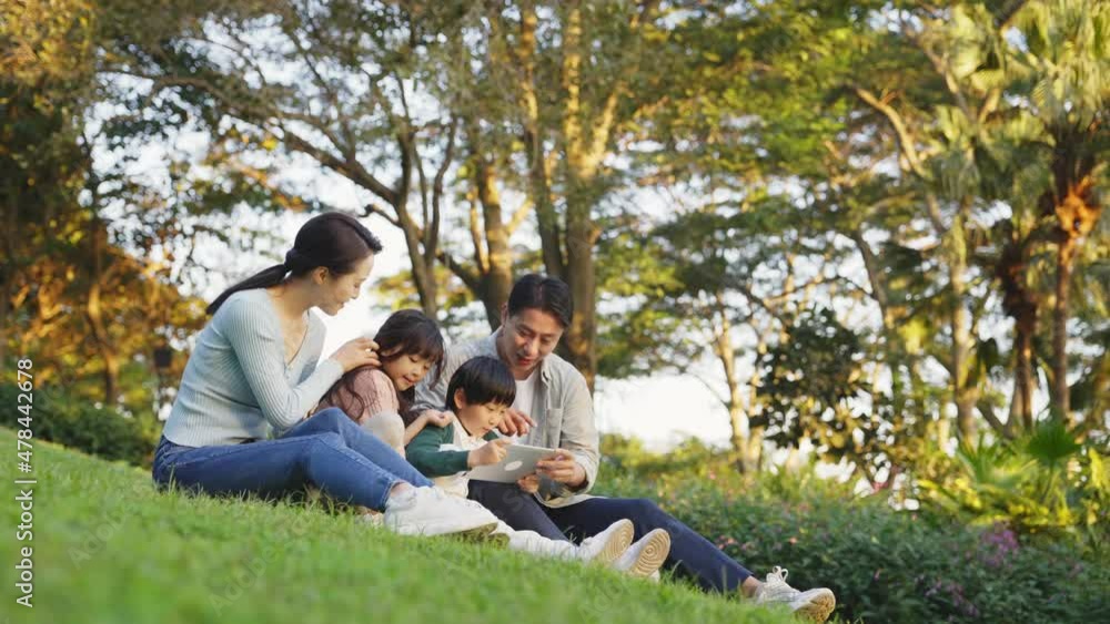 asian family with two children sitting on grass relaxing outdoors in city park asian family with two children sitting on grass relaxing outdoors in city park