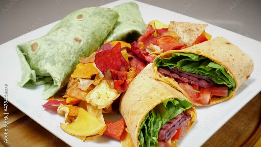 Full rotation shot of two BLT tortilla wraps cut in half side by side on a plate served with gourmet chips in a kitchen ready to serve. Bacon lettuce tomato sandwiches rolled up. Delicious low calorie Full rotation shot of two BLT tortilla wraps cut in half side by side on a plate served with gourmet chips in a kitchen ready to serve. Bacon lettuce tomato sandwiches rolled up. Delicious low calorie