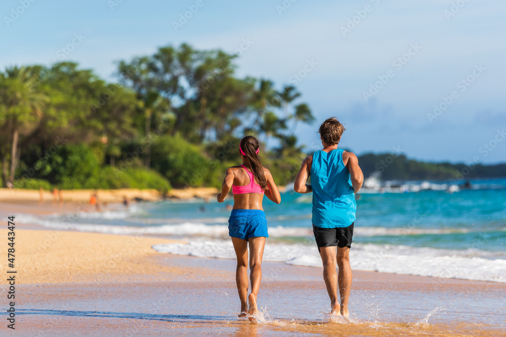 Couple runners athletes running on beach. Outdoor summer fitness exercise view from behind of woman and man jogging training together.