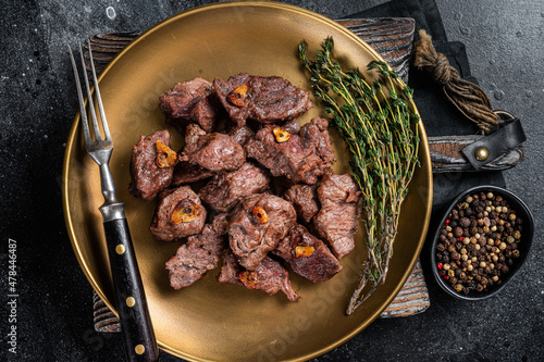 Chopped Grilled Diced Beef garlic steak on a plate with thyme. Black background. Top view