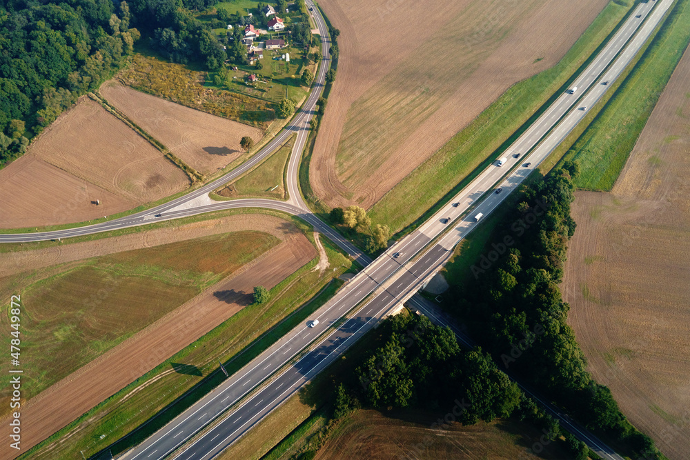 Fototapeta premium Highway crossroad with moving cars and trucks, aerial view. Asphalt road through countryside landscape