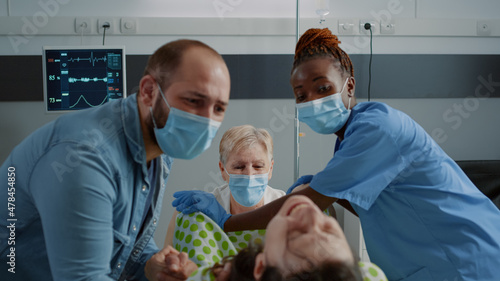 Close up of multi ethnic people delivering child in hospital ward. Doctor and african american nurse helping pregnant woman pushing for childbirth. Caucasian husband holding wife hand