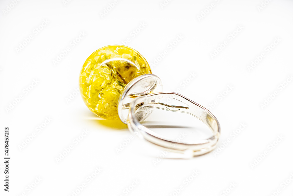 Back side of a yellow resin ring. Immortelle flowers in an epoxy resin sphere ball, silver colored base. Selective focus on the details, object isolated on white background. Back side of a yellow resin ring. Immortelle flowers in an epoxy resin sphere ball, silver colored base. Selective focus on the details, object isolated on white background.