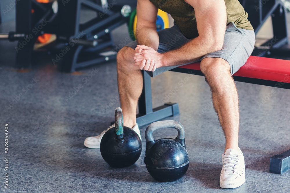 Naklejka premium Close up of athletic man sitting on a bench with kettlebells. The concept of fitness and bodybuilding