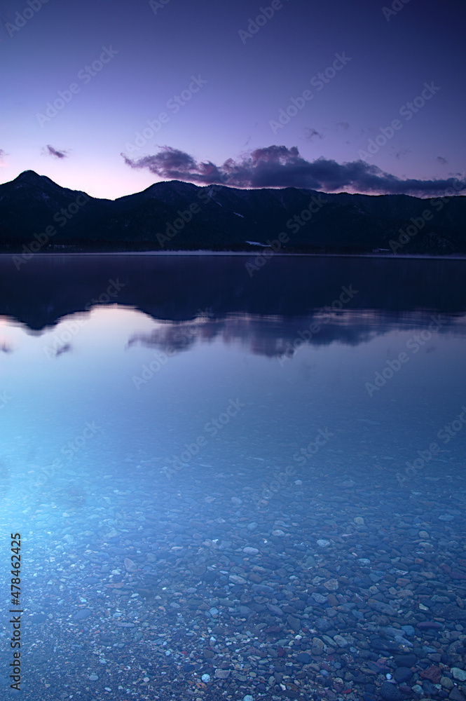 静水の湖面に山のシルエットと空を反射する黄昏の湖。日本の北海道の屈斜路湖。