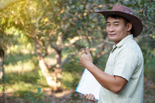 Εκτύπωση καμβά Asian male botanist holds  paper clipboard and thumbs up, stands at forest