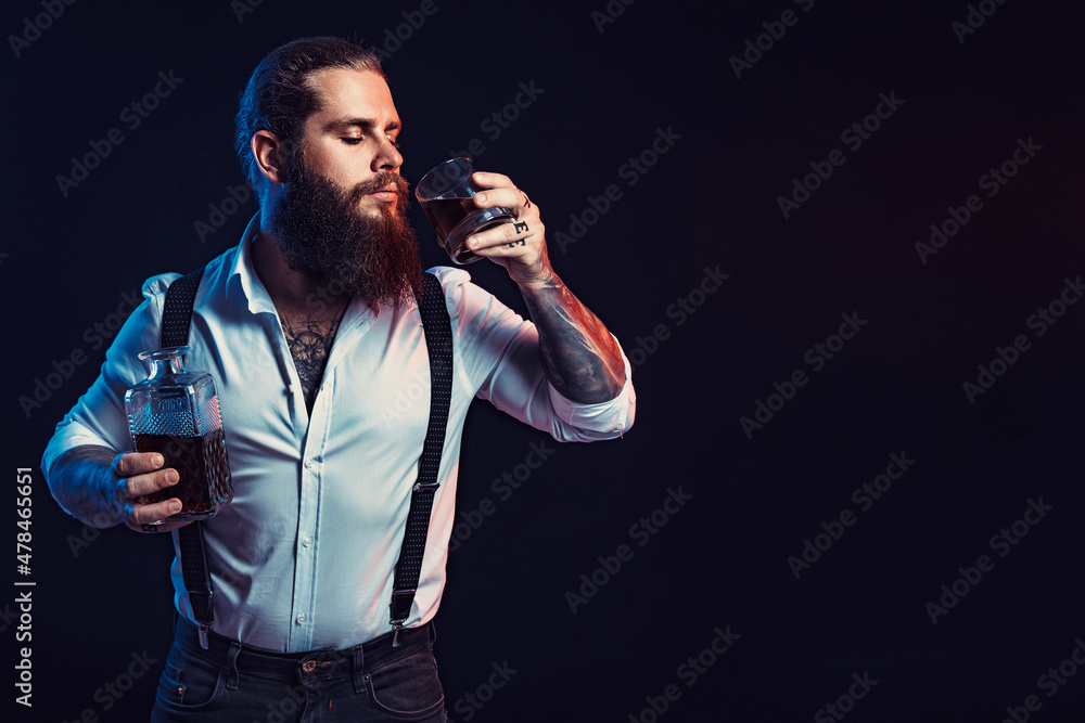 bearded man holds bottle of whiskey in his hand and drinks dressed in white shirt. Studio shot bearded man holds bottle of whiskey in his hand and drinks dressed in white shirt. Studio shot