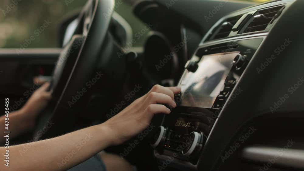 A young woman is sitting in the driver's seat. She is selecting music in the car's multimedia. She is using a touch screen. Close-up of her hands. 4K 50fps A young woman is sitting in the driver's seat. She is selecting music in the car's multimedia. She is using a touch screen. Close-up of her hands. 4K 50fps