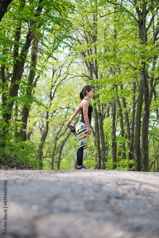 Female athlete stretching her thigh before a morning workout in the woods Female athlete stretching her thigh before a morning workout in the woods