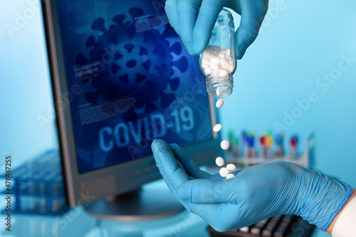Researcher with oral pill bottle of pharmaceutical antiviral drugs against covid-19 coronavirus. Doctor hand holds antiviral pills and background screen with illustration coronavirus covid-19 data. photo