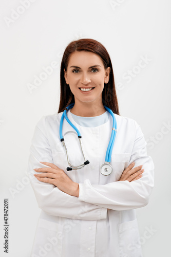 Smiling female doctor with arms crossed standing and looking at camera, isolated on white background. Medical occupation concept