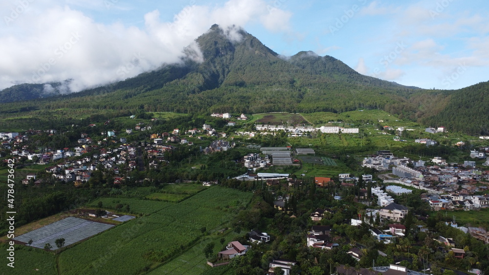 Drone photo of mountain view in Batu City, Indonesia surrounded with white clouds and small buildings