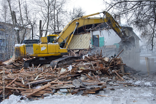 Building demolition. Excavator breaks old two-storey house. Industrial cityscape with destroy process.