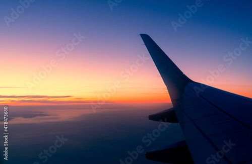 Wing of plane with sunrise skyline. Airplane flying in the sky. Scenic view from airplane window. Commercial airline flight. Plane wing above clouds. International flight. Travel abroad after covid-19