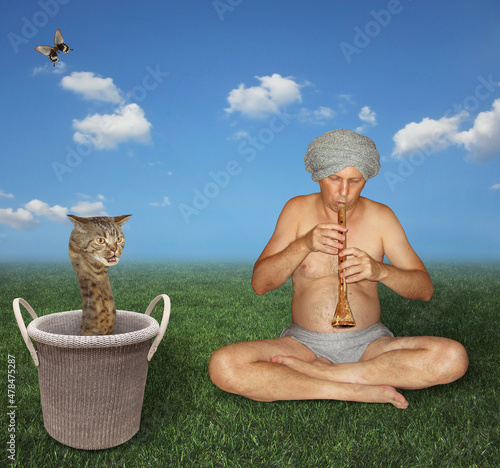 A man snake charmer in a turban is playing the flute for a beige cat snake in a knitted basket. photo