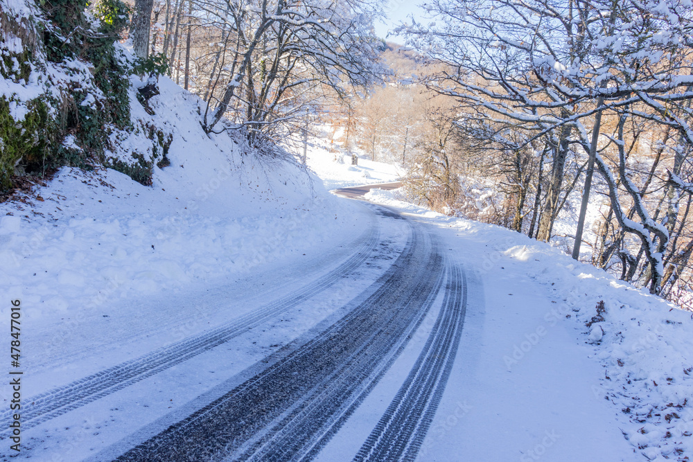 An empty road with a tricky left turn covered with snow. Tyre traces. Concept of road trip, extreme driving, safety on the roads, and environmental conservation. An empty road with a tricky left turn covered with snow. Tyre traces. Concept of road trip, extreme driving, safety on the roads, and environmental conservation.