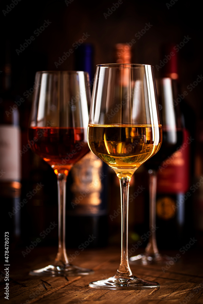 Red, white and rose wine in glasses on wooden background and collection of wine bottles, copy space