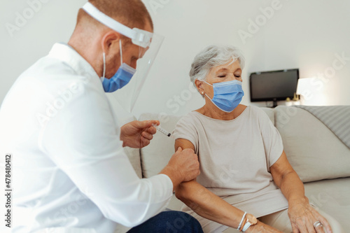 Beautiful senior woman in medical face mask getting Covid-19 vaccine at doctor s office. Professional nurse giving flu injection to patient. Vaccination  immunization campaign  disease prevention