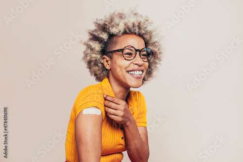 Cheerful afro latin american young woman with sticker on her arm showing she was vaccinated, isolated on beige background. Looking away.