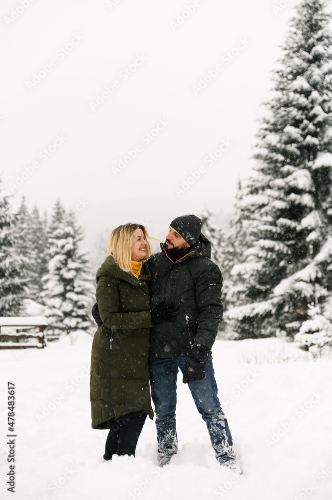 Attractive man and woman cuddling in the frosty forest. Adult couple in puffer jacket have fun on walk. Romantic date in winter time.Winter lovestory Attractive man and woman cuddling in the frosty forest. Adult couple in puffer jacket have fun on walk. Romantic date in winter time.Winter lovestory