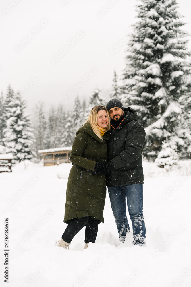 Attractive man and woman cuddling in the frosty forest. Adult couple in puffer jacket have fun on walk. Romantic date in winter time.Winter lovestory