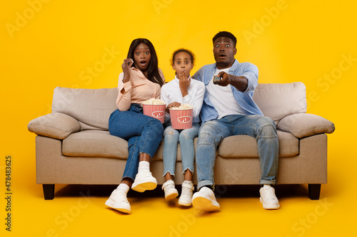 Surprised young family watching television with popcorn sitting on sofa