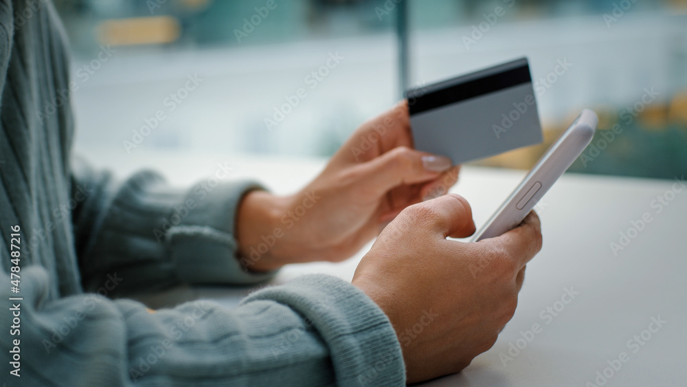 Close-up of female hands holding mobile phone and bank card shopping online. Unrecognizable woman pays for goods in web with smartphone enters secret account number book tickets makes order at table Close-up of female hands holding mobile phone and bank card shopping online. Unrecognizable woman pays for goods in web with smartphone enters secret account number book tickets makes order at table
