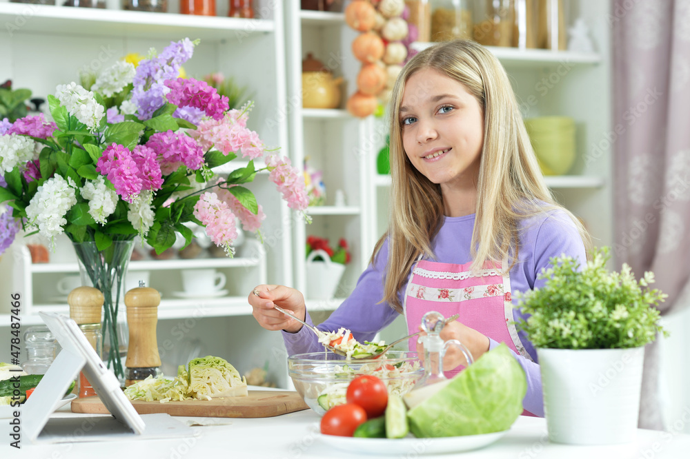 Cute little girl tasting fresh salad on kitchen