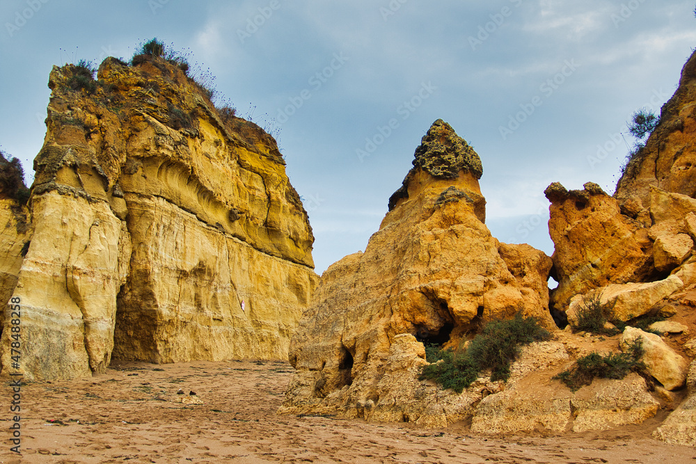 Yellow-red rock formations, eroded into jagged shapes, rise up from the sand. Faro, Algarve, Portugal
