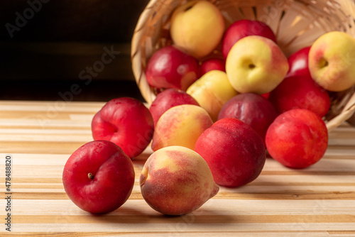 Plums and peaches, beautiful and juicy plums and peaches in a straw basket positioned on a rustic wooden surface, selective focus.