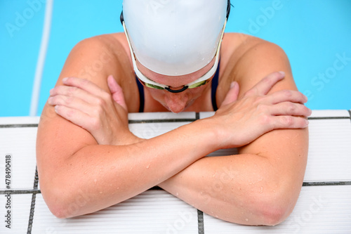 Female swimmer relaxes on the side of the swimming pool wearing a white swimming cap