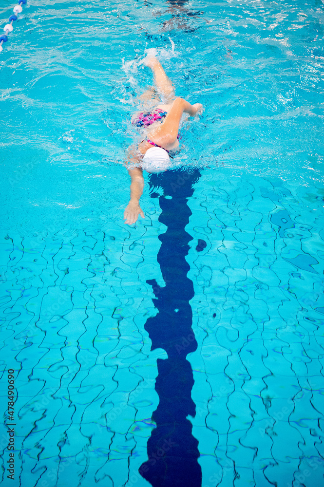 Swimmer swimming borstcrawl alone in an empty swimming pool while wearing a white swimming cap