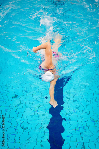 Swimmer swimming borstcrawl alone in an empty swimming pool while wearing a white swimming cap