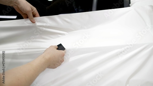 White protective film on the car. Polymeric protective outer coating. Auto detailing. Close-up of a hand smooths the film.