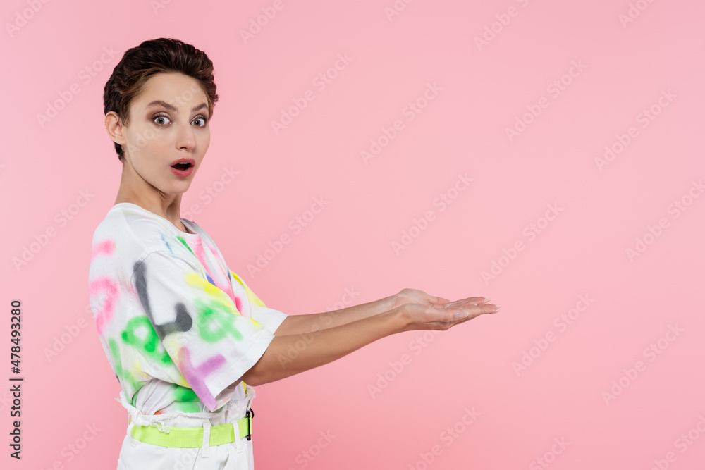 astonished woman in stylish t-shirt looking at camera and pointing with hands isolated on pink astonished woman in stylish t-shirt looking at camera and pointing with hands isolated on pink