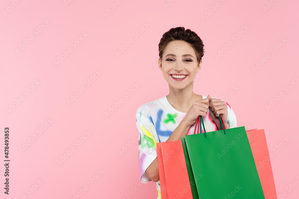 pleased brunette woman smiling at camera while holding shopping bags isolated on pink pleased brunette woman smiling at camera while holding shopping bags isolated on pink