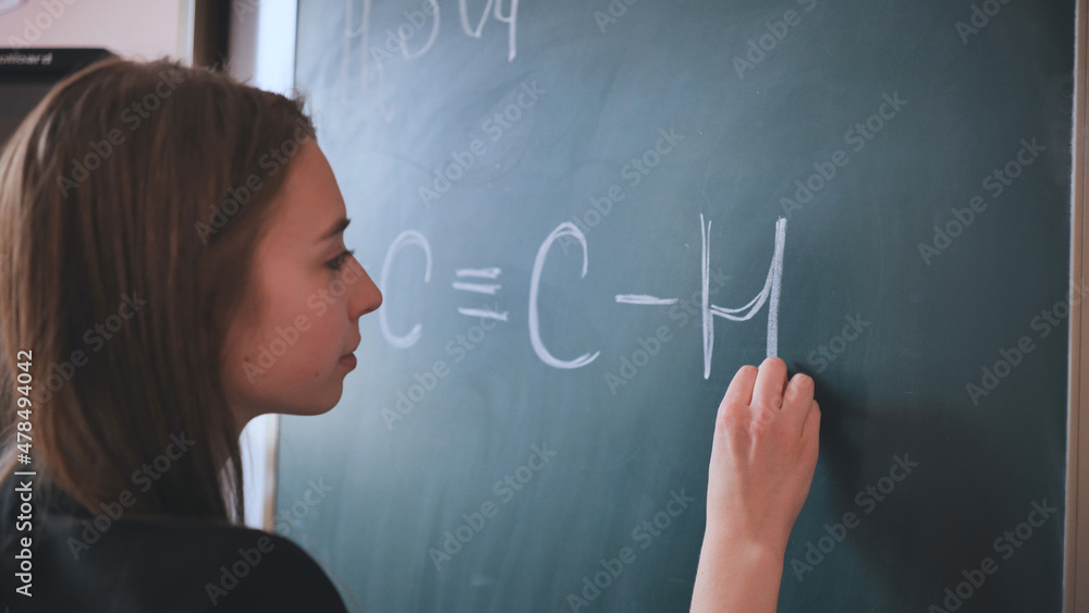 The girl is writing a chemical formula on the blackboard in the classroom.