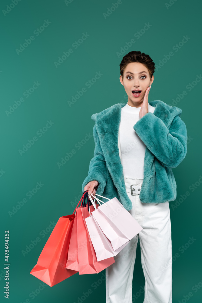 amazed woman in trendy clothes touching face while holding multicolored shopping bags isolated on green amazed woman in trendy clothes touching face while holding multicolored shopping bags isolated on green