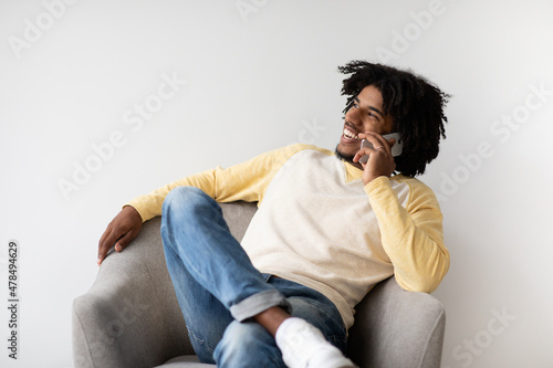 Mobile Communication. Cheerful Black Guy Talking On Cellphone While Relaxing In Armchair © Prostock-studio