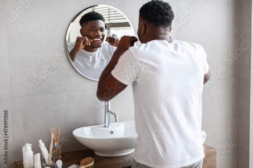 Foto African guy using tooth floss caring for teeth in bathroom