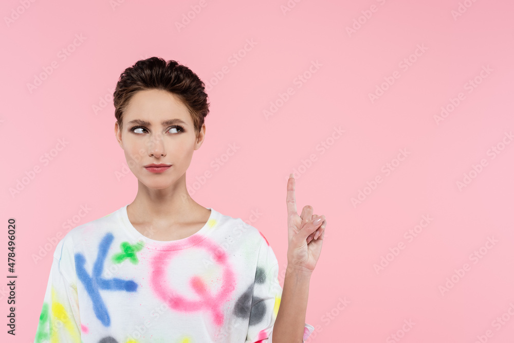 serious brunette woman in stylish t-shirt pointing up with finger isolated on pink serious brunette woman in stylish t-shirt pointing up with finger isolated on pink