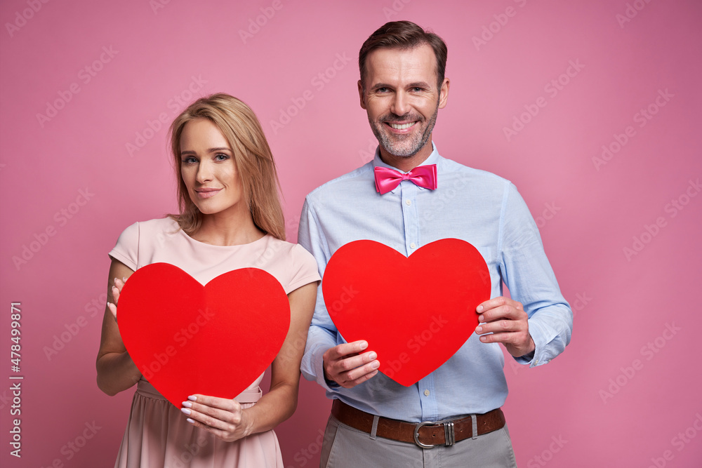 Portrait of caucasian ethnicity couple on pink background holding wooden hearts Portrait of caucasian ethnicity couple on pink background holding wooden hearts