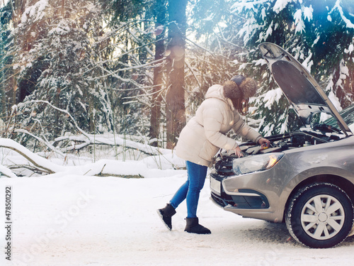 beautiful girl near the engine of a broken car on a winter snowy road. froze and calls for help
