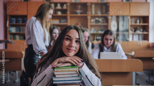 A student poses with textbooks at her desk in her class.